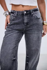 Jean de tiro medio en color negro lavado, con corte recto y amplio. Presenta detalles de tachas metálicas a lo largo de las costuras laterales y en la zona de los bolsillos delanteros.