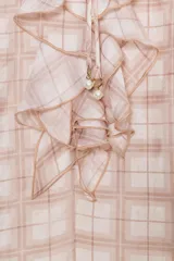 Blusa de manga larga abullonada con puños elásticos, cuello redondo con volantes y detalle de cordón ajustable en el escote pico. Presenta un estampado a cuadros en tonos blanco y rosado/marrón claro.