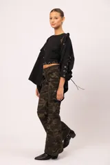 Camisa negra de microfibra con corte oversized. Presenta mangas con detalle de ojalillos y acordonado lateral, doble bolsillo frontal con solapa y botones metálicos. La parte trasera incluye diseño con tachas, ojalillos y cadena.