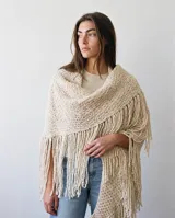 Ruana tejida en lana merino con diseño texturizado y flecos largos en los bordes.