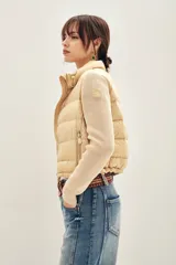 Campera puffer color beige con cuerpo acolchado y mangas tejidas de punto. Presenta cuello alto, cierre frontal y bolsillos laterales.