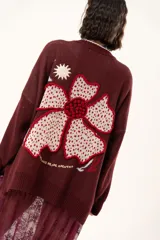 Saco tejido de punto en color bordó, con diseño de granada en la parte frontal y detalles bordados. Presenta cierre frontal con botones, cuello redondo y mangas largas con puños acanalados. El diseño incluye elementos artesanales y bordados a mano en la espalda.