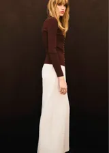 Pantalón de vestir color crudo, de corte recto y largo, con pliegues en los laterales y cierre delantero de cremallera metálica expuesta.