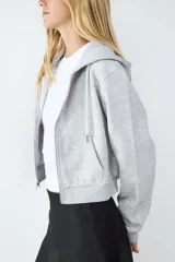 Campera con capucha y cierre frontal de cremallera, confeccionada en tejido gris melange con bolsillos estilo canguro y puños y bajo de canalé.
