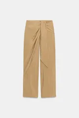 Pantalón de tiro bajo con diseño cruzado tipo pareo en el frente, que incluye un lazo decorativo. Presenta una silueta de pernera recta y cierre lateral con cremallera oculta.