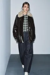 Chaqueta de efecto cuero color marrón oscuro con acabado brillante, cuello de solapa con aplicación de pelo sintético extraíble, manga larga con trabillas, bolsillos frontales de plastrón con solapa y cierre frontal con cremallera y botones a presión.