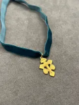 Gargantilla de cinta de terciopelo en color verde petróleo con dije de cruz dorada con la figura de Cristo y detalles grabados.