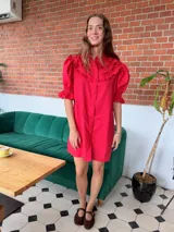 Vestido corto de lino color beige, con cuello alto, mangas cortas abullonadas con puños elásticos y volados en el pecho. Cuenta con cierre frontal de botones.