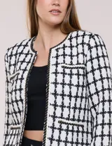 Chaqueta corta de corte estructurado confeccionada en tejido de tweed azul con patrón de cuadros, escote redondo sin solapa, frente abierto, bolsillos falsos y ribetes trenzados con hilos metalizados.