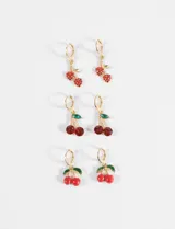 Set de tres pares de aros tipo argolla con dijes colgantes en forma de cerezas. El primer par presenta cerezas con incrustaciones de cristales rojos, el segundo par con cristales rojos grandes y hojas verdes, y el tercer par con cerezas esmaltadas en rojo y hojas verdes.