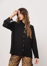 Camisa negra de cuello redondo con frunces y mangas largas con puños abiertos.