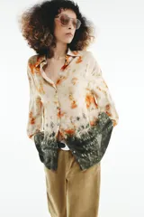 Camisa de manga larga con cuello solapa y cierre frontal con botones, con diseño tie-dye en tonos beige, naranja y verde oscuro en el sector inferior.