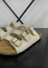 Sandalias beige con tres tiras horizontales ajustables con hebillas plateadas, plantilla de corcho y suela plana.