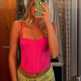 Corset o top estilo bustier color fucsia, con tirantes finos y detalles de encaje o tejido calado. Presenta un escote festoneado y un corte ajustado que termina en pico en la parte inferior.