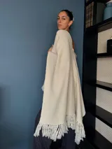 Ruana tejida a mano en punto arroz con lana merino, presenta un diseño envolvente con flecos en los extremos.