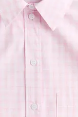 Camisa de corte holgado confeccionada en popelina de algodón, con cuello clásico, cierre frontal de botones, hombros caídos y bolsillo de parche en el pecho. Presenta mangas largas con puños abotonados, canesú en la espalda y bajo redondeado con aberturas laterales, siendo ligeramente más larga en la parte posterior.