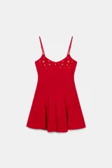 Vestido corto rojo, ajustado en el busto y con falda acampanada. Tiene tirantes finos ajustables y apliques metálicos dorados en forma de corazón y redondos en el escote.