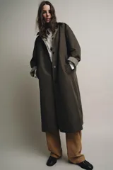 Trench reversible de corte recto con cuello de solapa y aplicación de pelo sintético extraíble. Presenta cierre frontal con botones, manga larga y bolsillos laterales ocultos en las costuras.