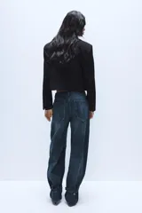 Blazer corto de corte recto con cuello de solapa, manga larga y hombreras. Presenta un diseño minimalista sin botones y forro interior a tono.
