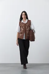 Chaleco tejido color marrón con bordados artesanales de motivos florales y geométricos en color crema. Presenta cuello redondo, cierre frontal con botones y diseño sin mangas.