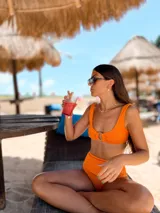 Top de bikini color naranja, con textura acanalada, escote redondo y tirantes anchos. Presenta una argolla decorativa en el centro del busto y se ata en la espalda.