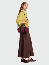 Bolso tipo "duffle" o "barrel bag" de Longchamp, modelo Le Pliage Energy, color bordó con detalles en negro. Cuenta con una correa ajustable y asas cortas.