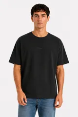 Remera de manga corta color negro, con cuello redondo y diseño holgado. Presenta un pequeño texto estampado en el centro del pecho.