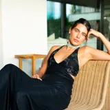 Vestido largo con estampado tie-dye en tonos violeta y fucsia, escote en V con detalles bordados dorados, cut-outs laterales bajo el busto y tirantes finos que se cruzan y atan en la espalda.