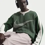 Buzo tejido de punto Nike, con diseño de rayas verticales en color verde y blanco. Presenta un logo Swoosh grande integrado en el tejido en el frente y un pequeño logo bordado en el puño. Posee cuello redondo y puños acanalados.