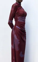 Vestido midi de microtul con diseño drapeado lateral, cuello alto y mangas largas. Presenta un estampado tipo tie-dye en tonos bordó y violeta.