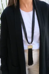 Collar largo de múltiples hilos negros con dije rectangular de textura rugosa en tono dorado y fleco largo de hilos negros colgante.