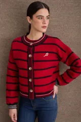 Cardigan de punto con diseño a rayas horizontales rojas y negras, cuello redondo y cierre frontal con botones. Presenta mangas largas con puños acanalados y un pequeño bordado de una raqueta de tenis en el pecho.