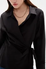 Camisa blanca de algodón con diseño cruzado y anudado lateral, cuello camisero y mangas largas con puños.