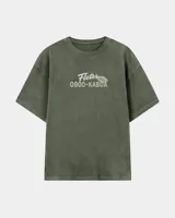 Remera oversize verde militar con efecto lavado, cuello redondo y estampa frontal con el texto "Fletes 0800-KABOA".