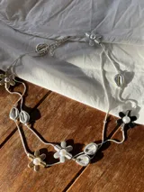 Collar largo plateado con dije de flores blancas, negras y doradas, y dijes de conchas plateadas.