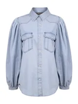 Blusa de jean celeste claro con mangas largas abullonadas, cuello camisero, bolsillos frontales con tapeta y cierre de broches metálicos a presión.