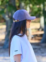 Gorra unisex de color beige con visera curva y aplique de cuero con logo grabado en el frente. Cuenta con hebilla metálica posterior para ajuste.