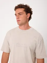 Remera holgada de algodón color beige con lavado ácido, cuello redondo ancho y diseño de tres pequeños círculos estampados en el pecho.