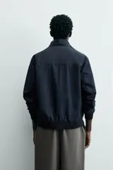 Cazadora azul marino de corte regular fit, confeccionada en tejido técnico repelente al agua. Presenta cuello subido, manga larga, bolsillos de vivo en cadera, bolsillo interior y acabados en rib en puños y bajo. Cierre frontal de cremallera oculta por solapa con botones a presión.