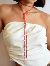 Corbatín tipo choker de gamuza roja con diseño de tiras largas que caen al frente, decoradas con pequeñas estrellas metálicas plateadas.