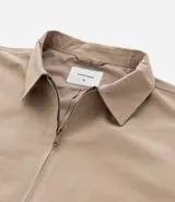 Campera de sarga color beige con cuello inglés, cierre frontal de cremallera, mangas largas y bolsillos laterales. Diseño minimalista y versátil con forro interior.
