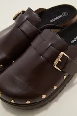 Suecos negros de estilo casual con acabado en eco cuero, detalle de hebilla metálica ajustable en el empeine y tachas decorativas en el contorno de la suela. Presentan una base de corcho y suela de goma dentada.