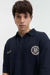 Remera polo color crema con logo bordado en el pecho, de corte amplio y mangas cortas.