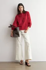 Blusa de color rojo con cuello mao y escote en V, mangas tres cuartos abullonadas con puños elásticos y detalles de bordado floral en el pecho y las mangas.
