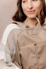Mochila compacta de color beige, con compartimento principal con cierre, bolsillos laterales y bolsillo frontal con cierre oculto. Cuenta con correas regulables y acolchonadas y asa superior.