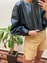 Campera de cuero con silueta oversize y corte levemente corto. Presenta cierre frontal metálico, cuello a la base y mangas amplias con detalles trenzados y recortes que aportan textura.