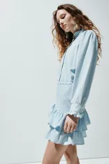 Pollera mini confeccionada en denim de algodón celeste, con cuerpo ajustado en punto smock y doble volante al bies en el bajo.