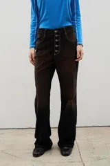 Pantalón de tiro alto confeccionado en pana, con corte recto y efecto gastado en degradé que transiciona de tonos oscuros a ocre. Presenta un cierre frontal con botones visibles y costuras a contratono.