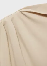 Camiseta color beige con cuello alto asimétrico, sin mangas y detalles fruncidos. Tejido fluido y diseño recto.