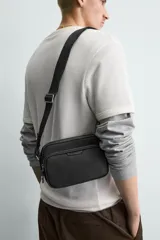 Bandolera negra rectangular de tela técnica con correa ajustable y extraíble.